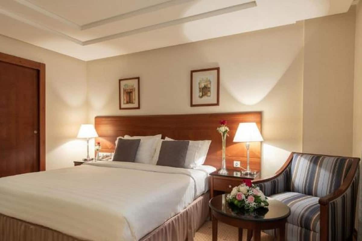Une chambre d’hôtel avec un grand lit, deux tables de chevet avec des lampes, une chaise et deux tableaux encadrés au mur.
