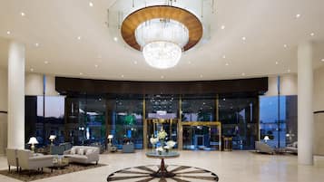 A spacious lobby with a grand chandelier, comfortable seating, and a large glass entrance.
