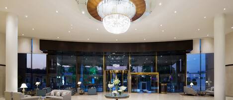 A spacious lobby with a grand chandelier, comfortable seating, and a large glass entrance.