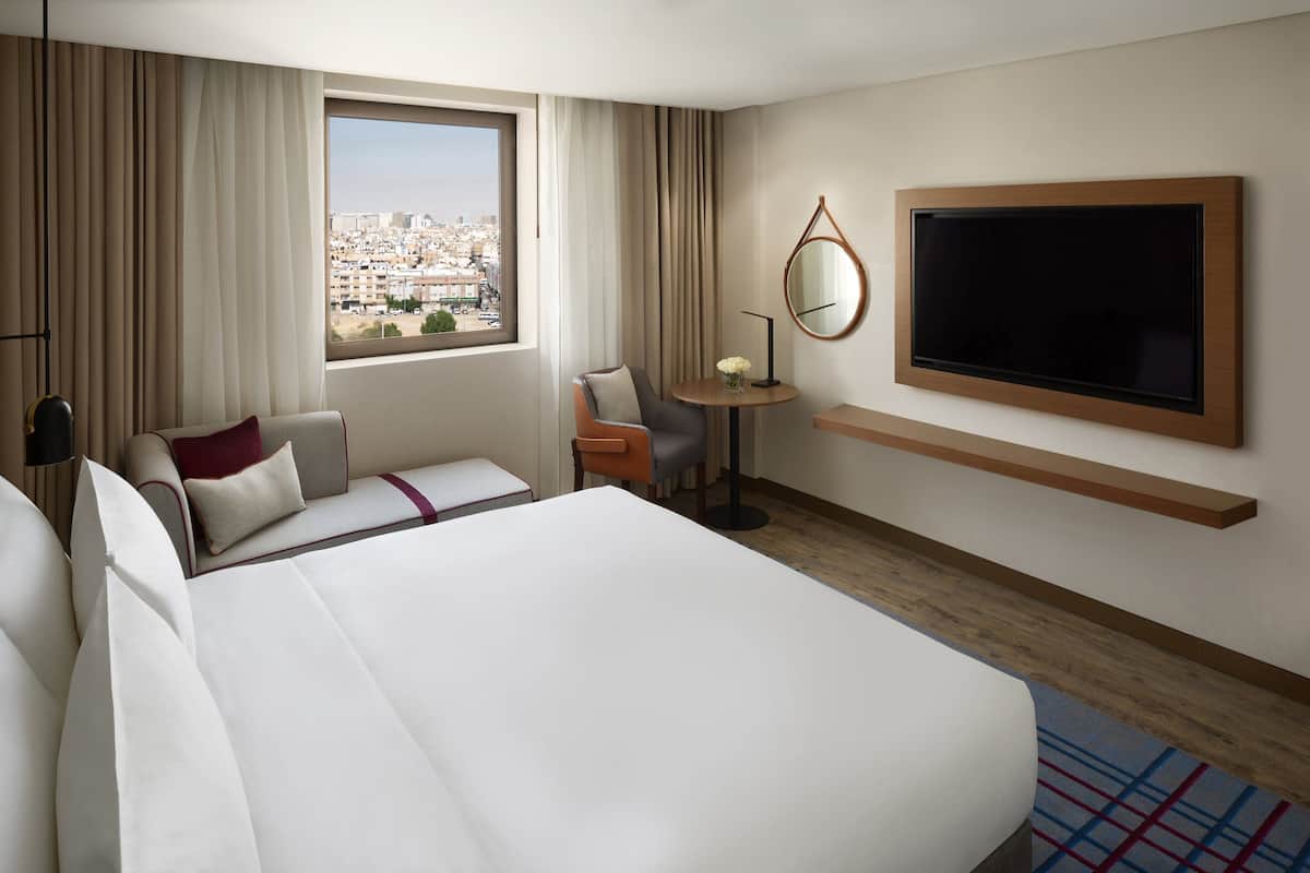 Une chambre d’hôtel avec un grand lit, un bureau, une chaise, une télévision et une vue sur la ville.
