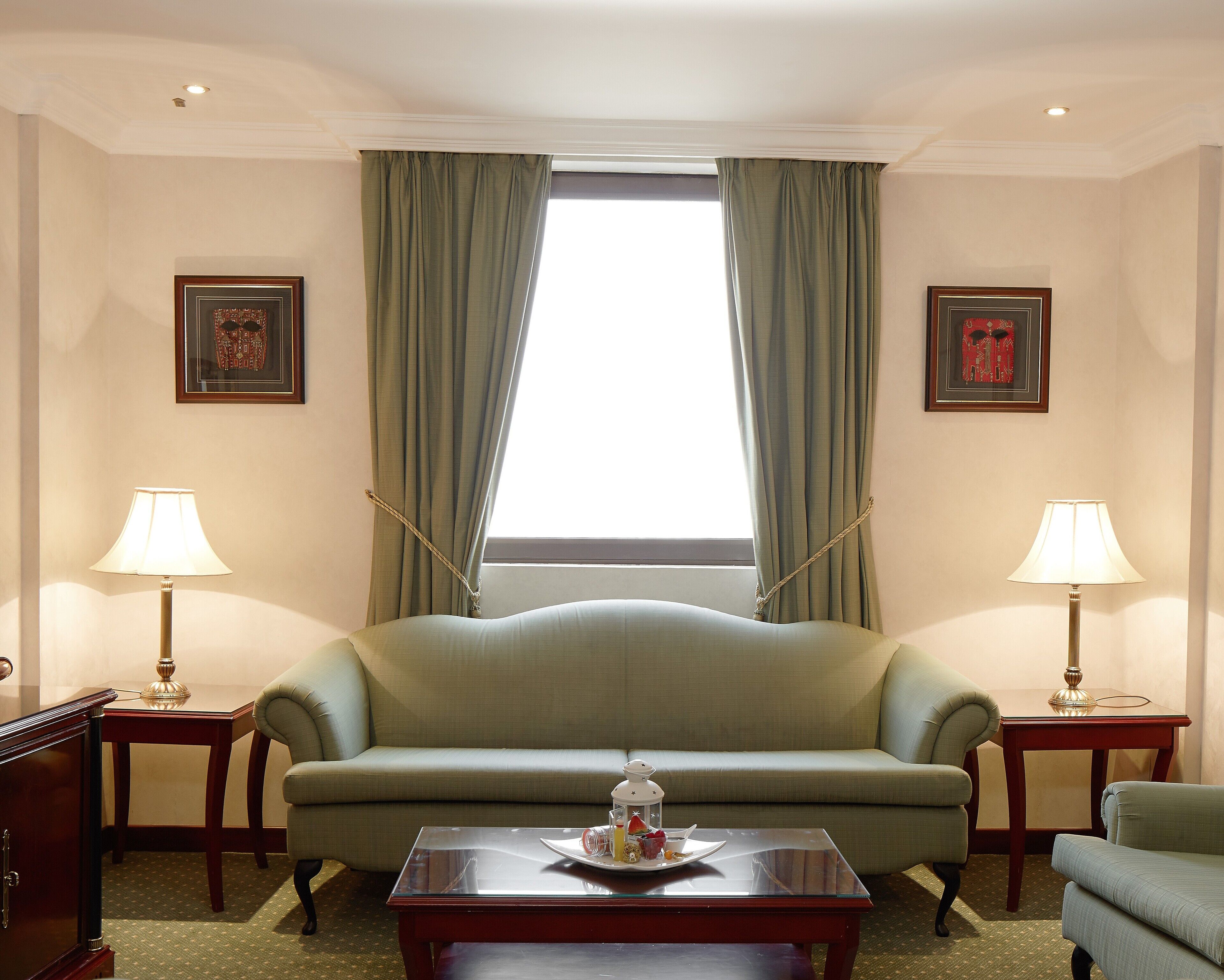 A room with a sofa, two lamps, a coffee table, and a window with curtains.