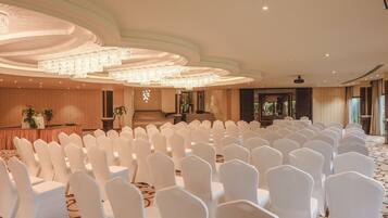 Un salón de conferencias con filas de sillas blancas, un escenario con un atril y una gran lámpara de cristal.