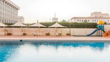 A swimming pool with a slide, lounge chairs, and umbrellas.