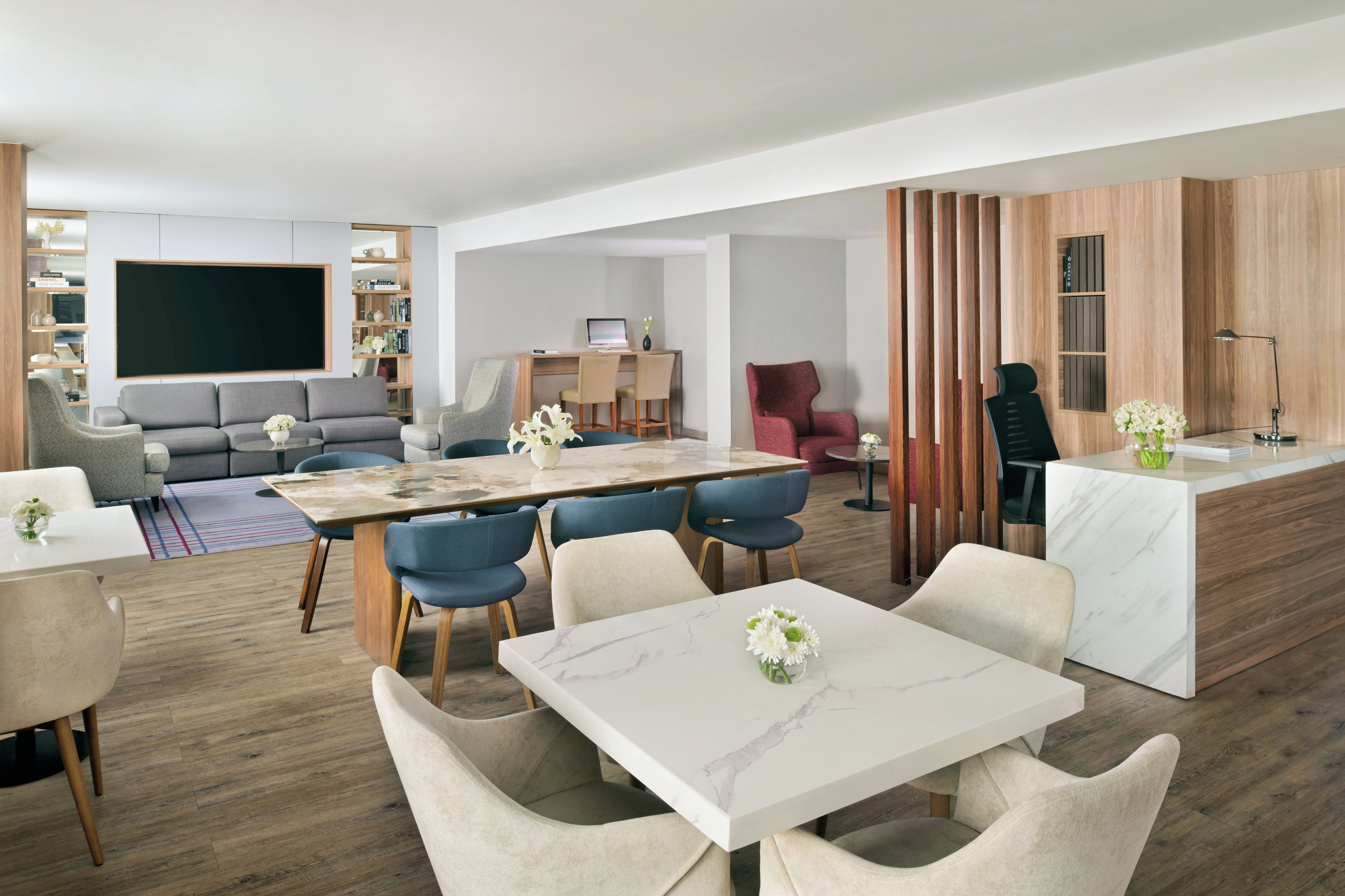 Un soggiorno moderno con una grande TV a schermo piatto, una zona pranzo con tavolo in marmo e un angolo cottura con piano di lavoro in legno.