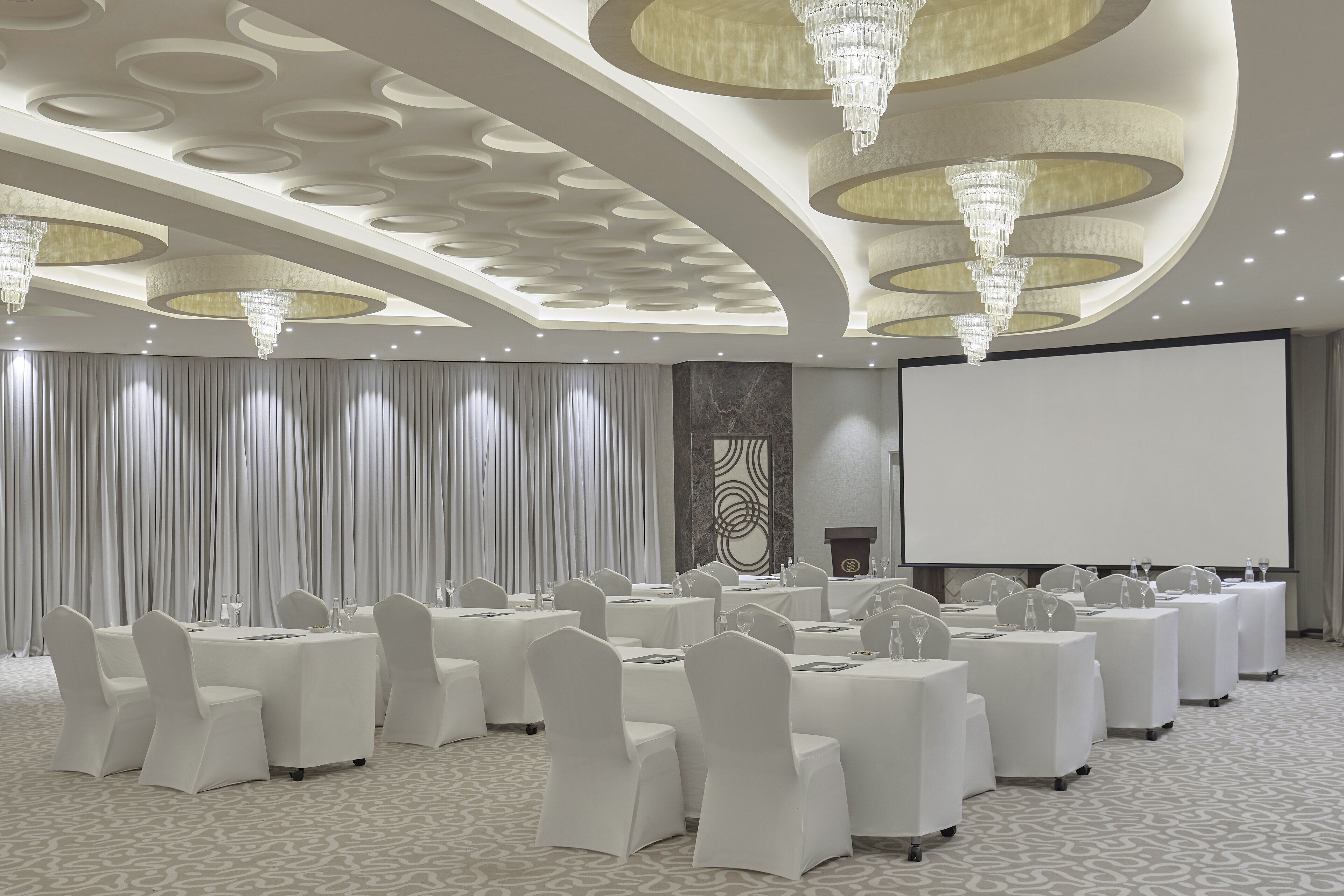 A conference room with round tables, white chairs, and a large screen.