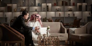 A man and a woman sitting on a sofa in a room with a bookshelf and a coffee table. - Crowne Plaza Riyadh Palace by IHG (Riyadh)