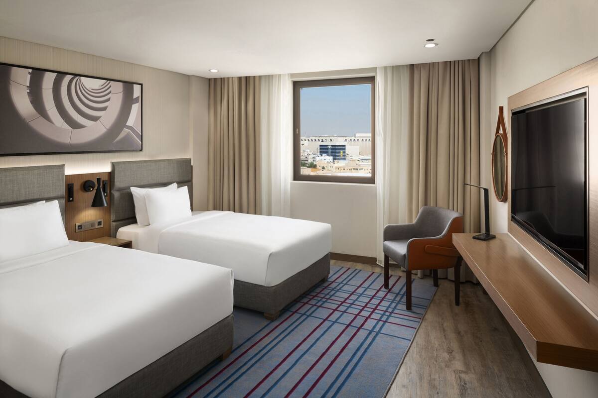 Une chambre d’hôtel avec deux lits, un bureau, une télévision et une grande fenêtre donnant sur la ville.