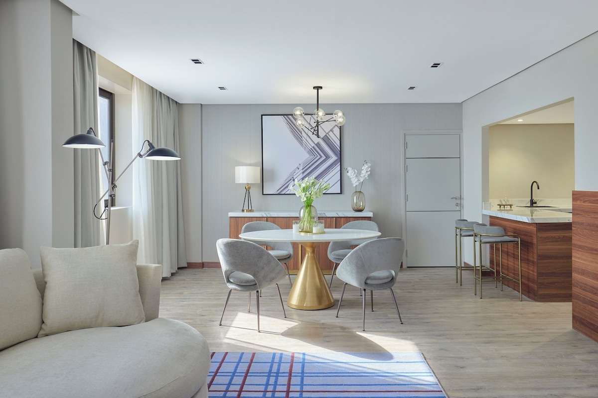 A modern living room with a sofa, a round table, and two bar stools.