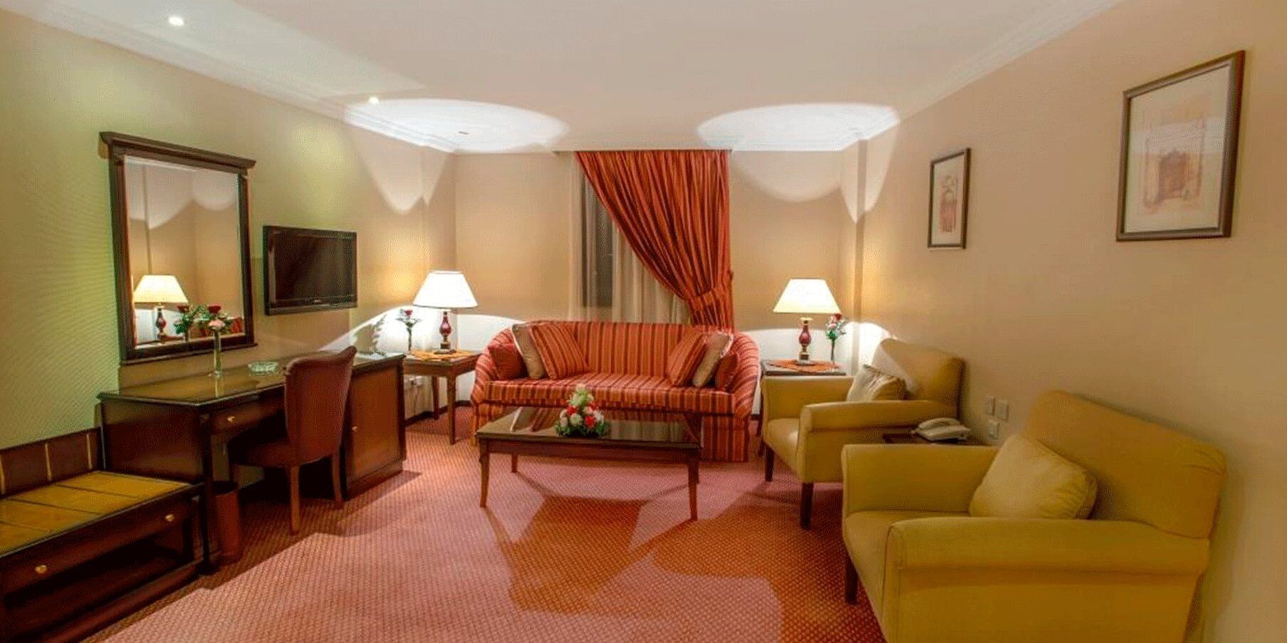 Ein Hotelzimmer mit einer Couch, Sesseln, einem Schreibtisch und einem Fernseher.