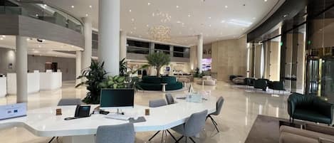 A spacious lobby with a reception desk, seating area, and a large central plant.