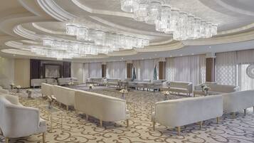 A spacious, elegantly decorated room with a patterned carpet, multiple seating arrangements, and a large chandelier.