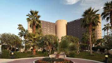 A hotel with a central circular garden, palm trees, and a modern building facade.