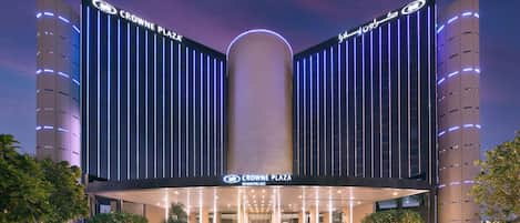 Un hotel moderno con una entrada destacada, iluminación vertical y un elemento cilíndrico central.