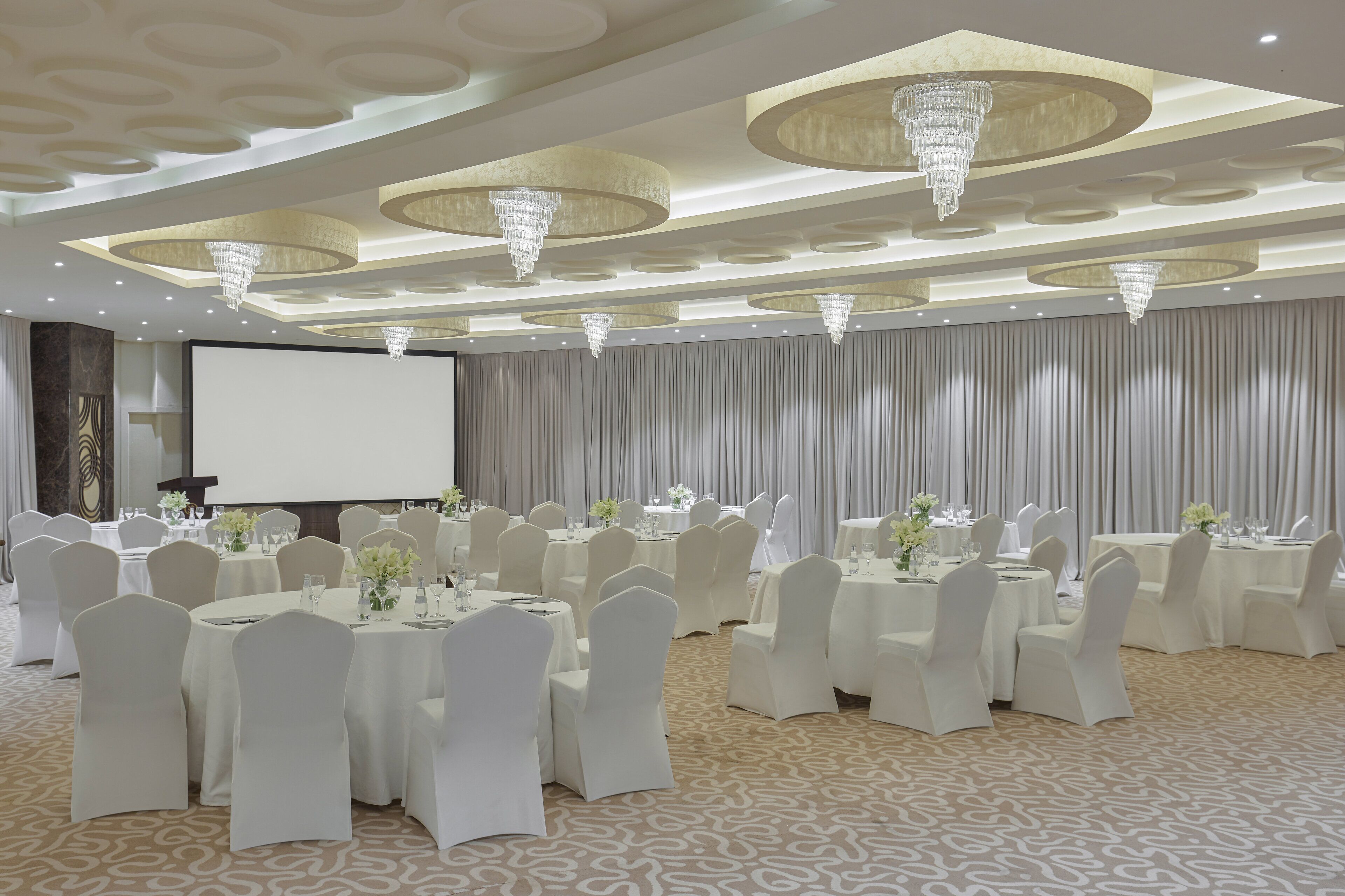 Een balzaal met ronde tafels, witte stoelen en kroonluchters.