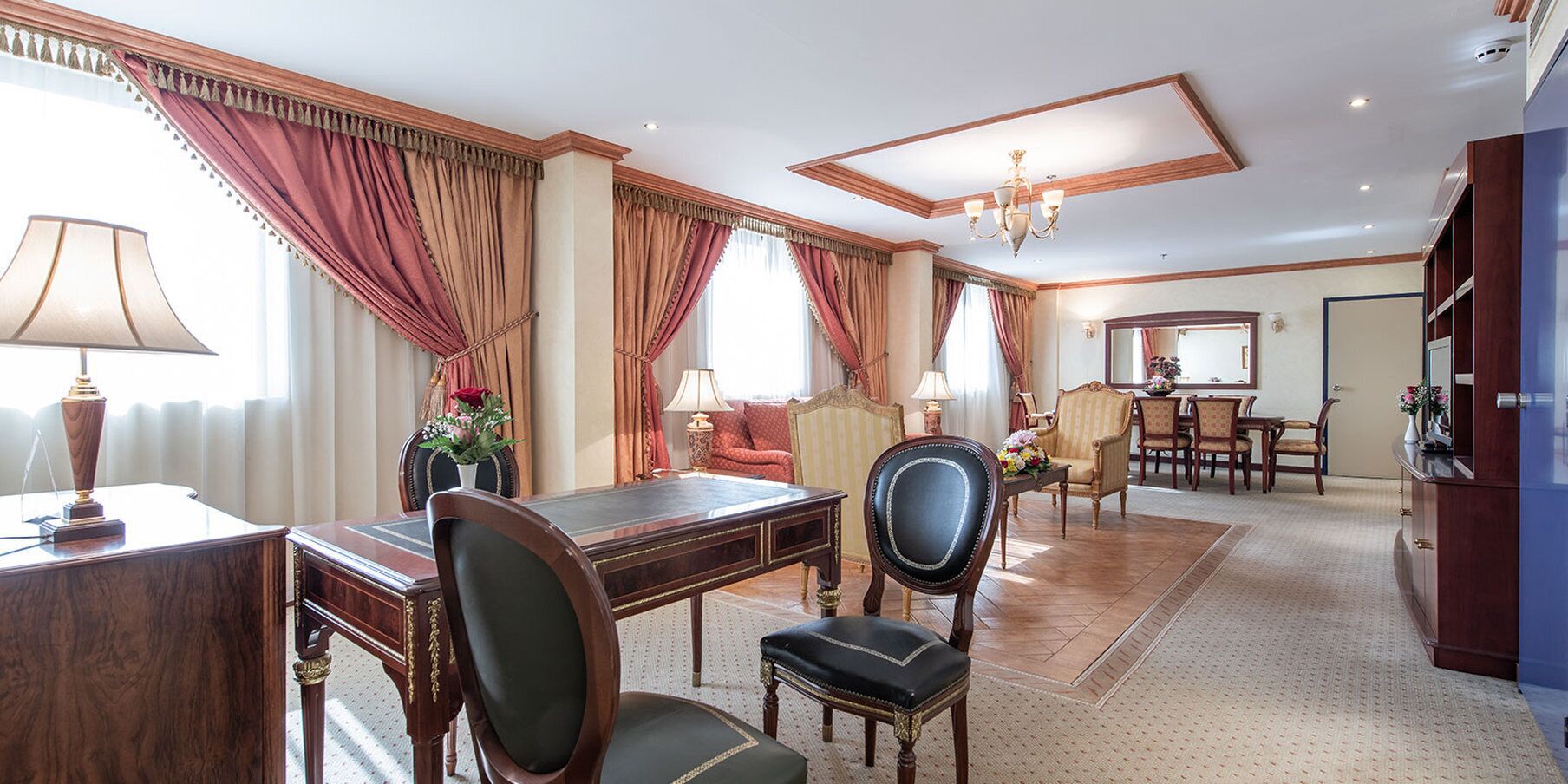 Ein Hotelzimmer mit Essbereich, Schreibtisch mit Lampe, Sofa und einer Kandelaber.