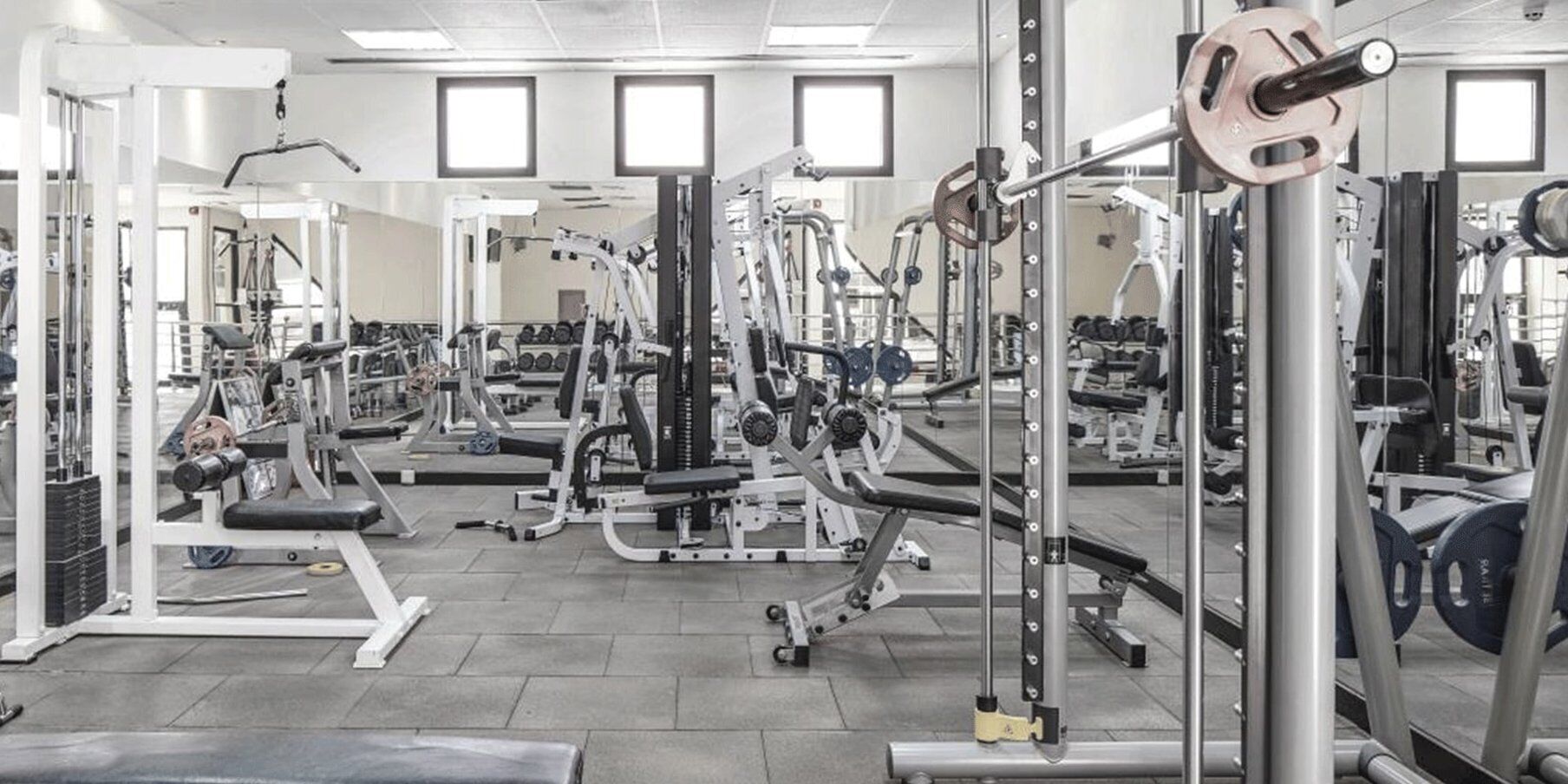 A gym with various exercise machines, mirrors, and a tiled floor.