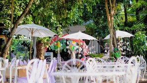 An outdoor seating area with white metal chairs and tables, surrounded by trees and covered by white umbrellas. - Chayada Garden House and Resort Hotel (Nakhon Ratchasima)