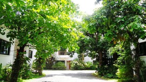 A pathway flanked by lush greenery and white buildings with a central entrance. - Chayada Garden House and Resort Hotel (Nakhon Ratchasima)