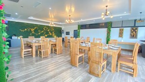 A spacious dining area with wooden tables and chairs, a green wall with decorative elements, and ceiling lights. - Chayada Garden House and Resort Hotel (Nakhon Ratchasima)