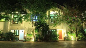 A two-story building with multiple windows and doors, surrounded by lush greenery and illuminated by ambient lighting. - Chayada Garden House and Resort Hotel (Nakhon Ratchasima)