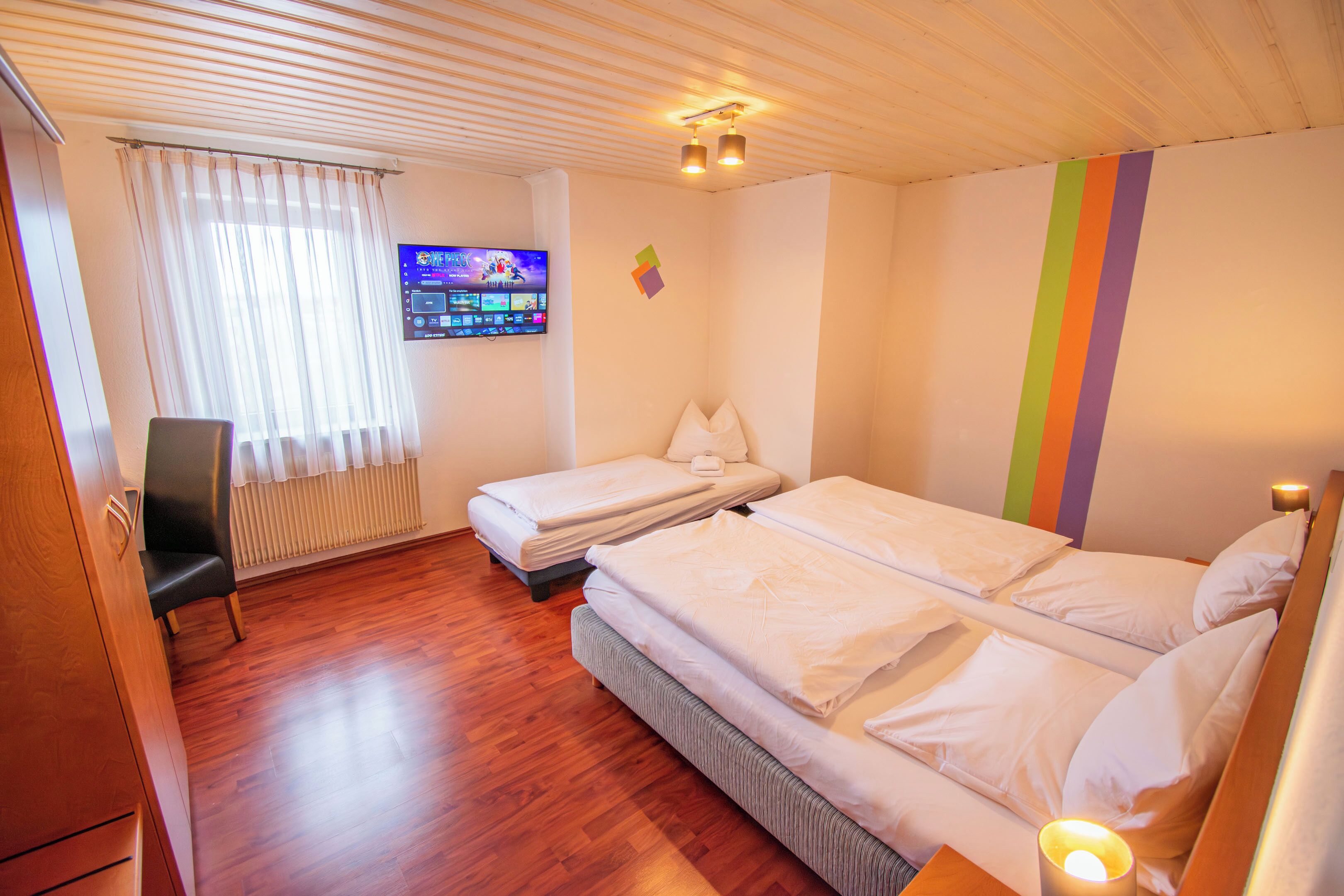 Hotellihuone, jossa on kaksi sänkyä, televisio, työpöytä ja ikkuna, jossa on verhot.