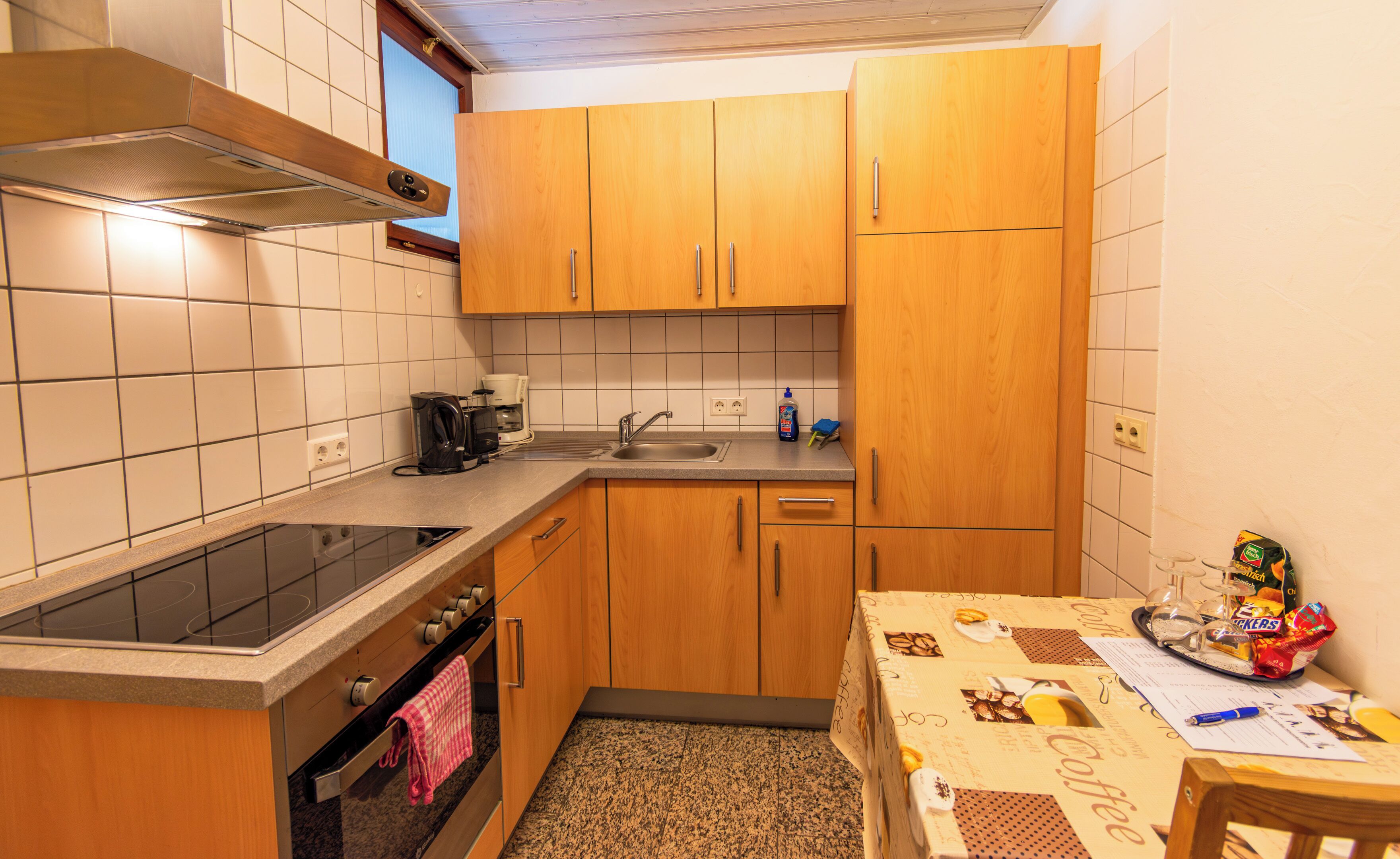 Een kleine keuken met houten kastjes, een inbouwoven, een kookplaat en een koffiezetapparaat.