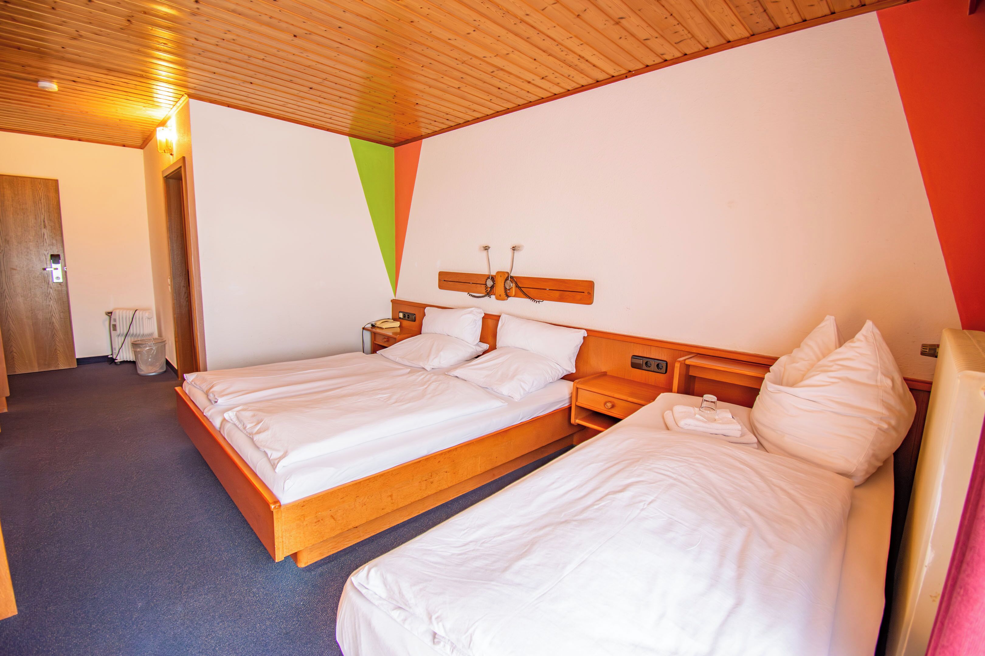 Une chambre d’hôtel avec deux lits, des têtes de lit en bois, un plafond en bois et un mur sobre.