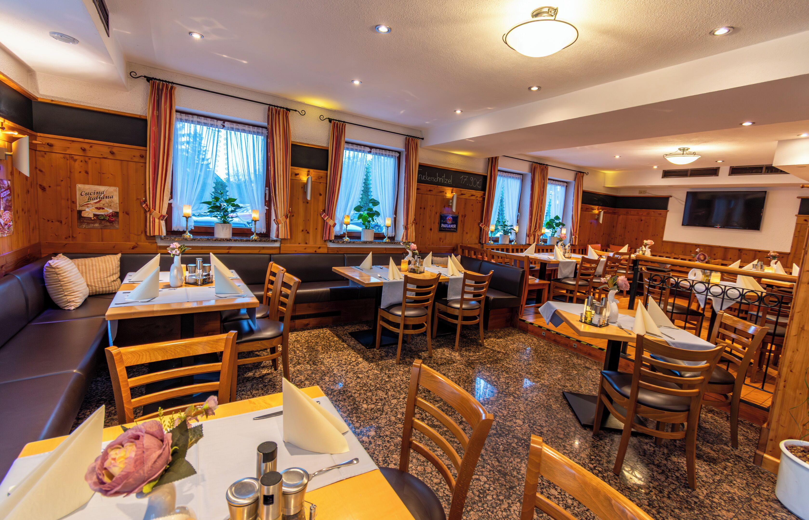 A restaurant with wooden paneling, multiple seating areas including tables and booths, and large windows with curtains.