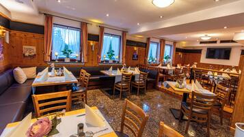 A restaurant with wooden paneling, multiple seating areas including tables and booths, and large windows with curtains.
