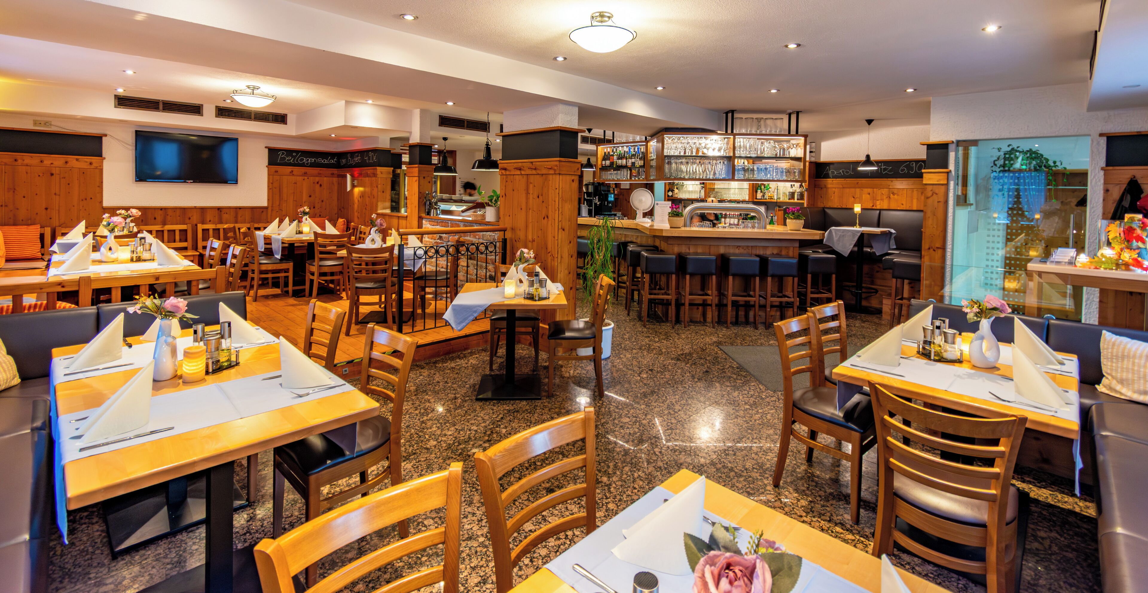 Ein Restaurant mit mehreren Tischen, St ühlen, einer Bar und einem an der Wand befestigten Fernseher.