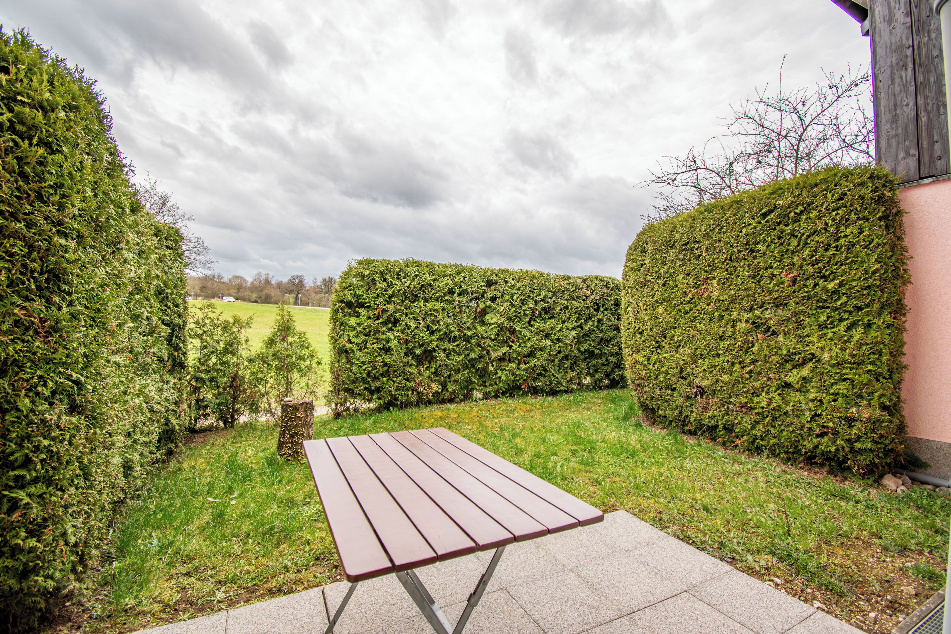 Une terrasse avec une table, entourée de haies bien entretenues et d’une pelouse.
