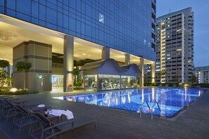 A modern hotel with a swimming pool, outdoor seating, and a glass facade.