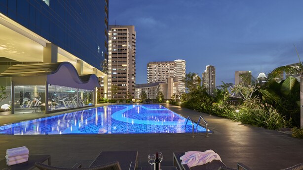 A rooftop pool with lounge chairs and a table, surrounded by modern buildings and greenery. - Hotel Boss (Singapore)