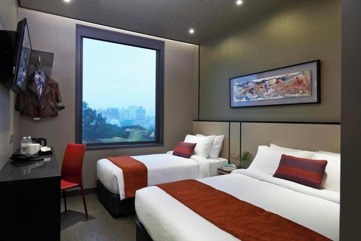 A hotel room with two beds, a desk, a chair, a TV, and a large window with a city view.