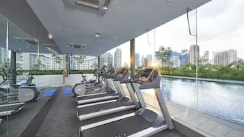 Un gimnasio moderno con cintas de correr, bicicletas estáticas y vista a la ciudad desde la piscina.