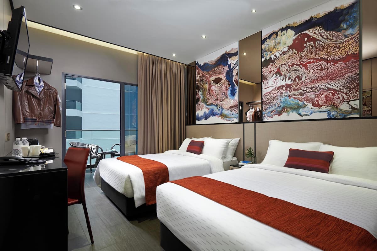 A hotel room with two beds, a desk, a chair, a TV, and large abstract paintings on the walls.