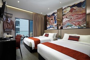 A hotel room with two beds, a desk, a chair, a TV, and large abstract paintings on the walls.
