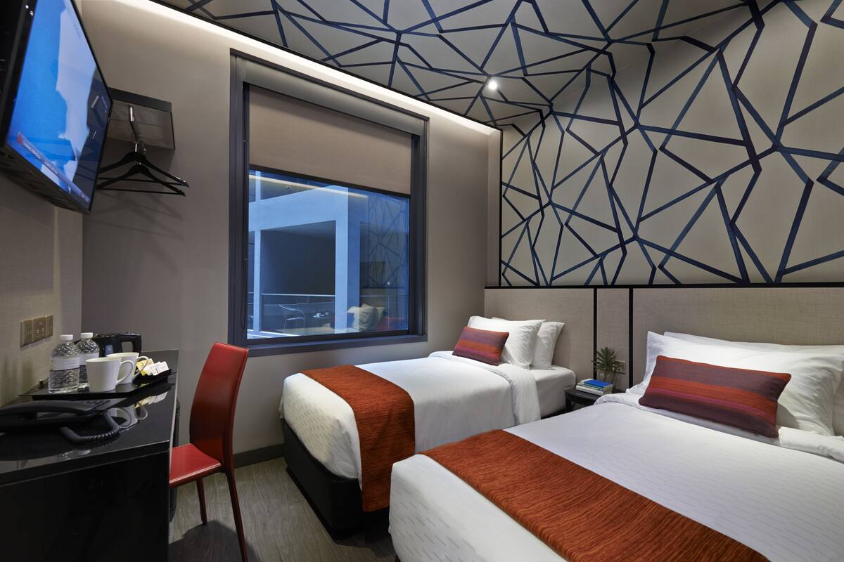 A hotel room with two beds, a desk with a telephone, a chair, and a TV mounted on the wall.
