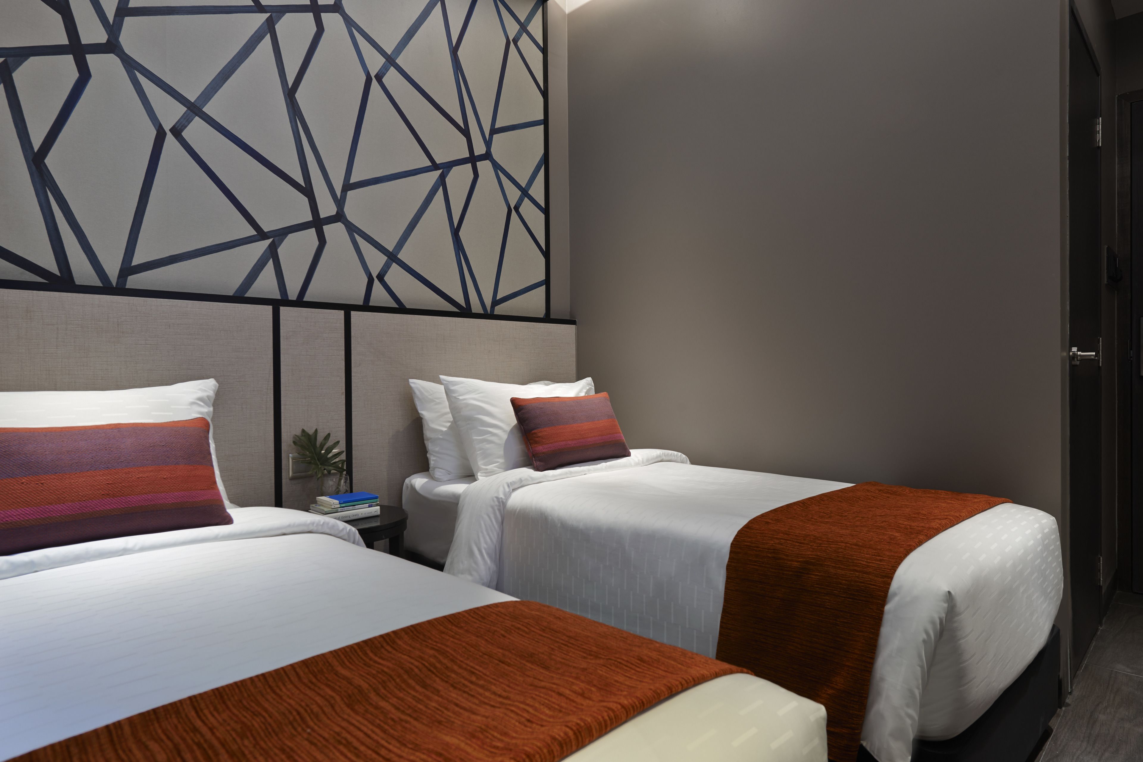 A hotel room with two beds, a geometric wall design, and a modern aesthetic.