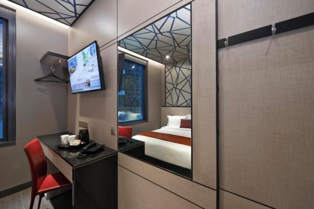 A hotel room with a bed, a desk with a chair, a television, and a window.