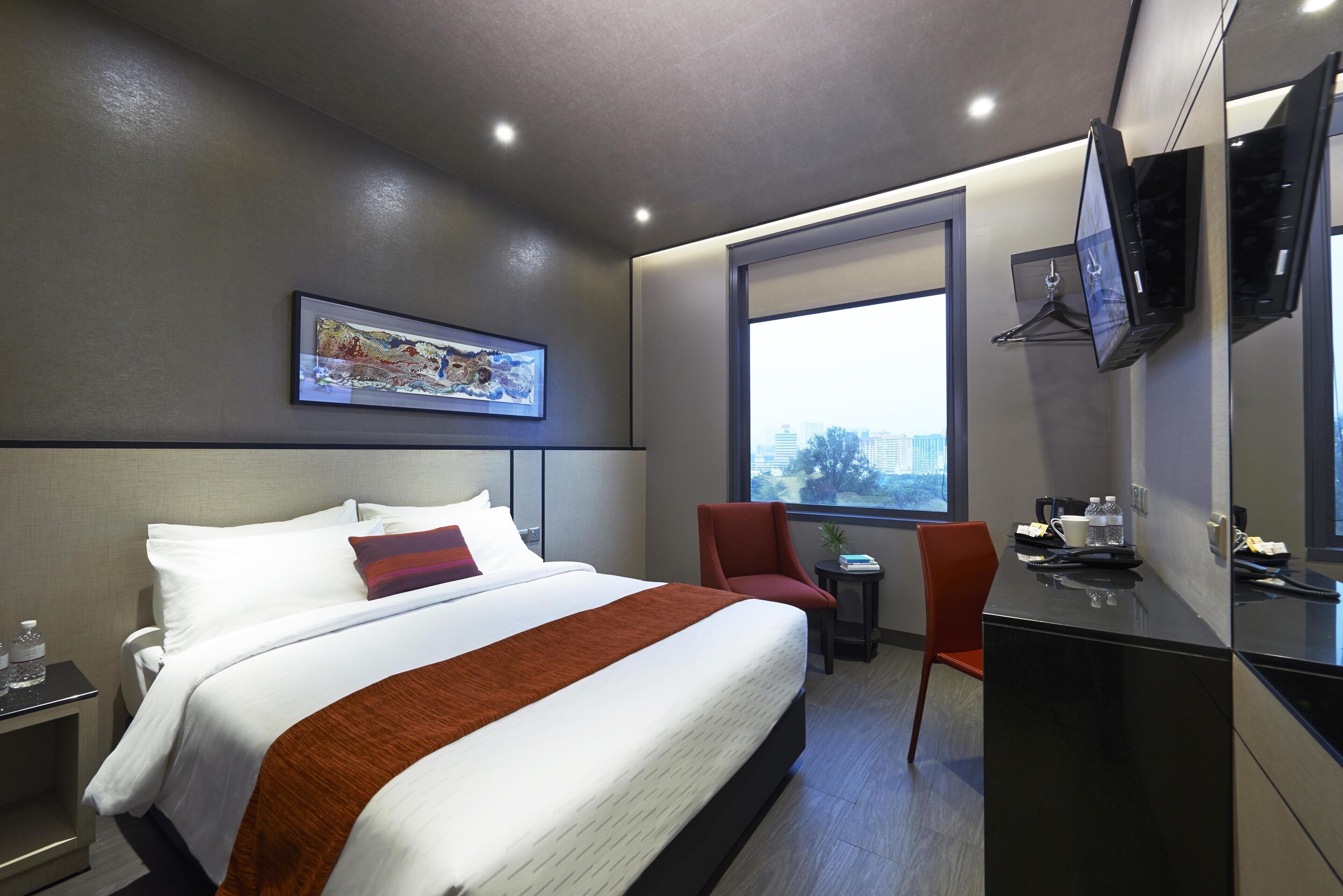 Ein modernes Hotelzimmer mit einem großen Bett, einem Schreibtisch, einem Stuhl, einem Fernseher und einem Fenster mit Blick auf die Stadt.