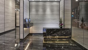 A modern reception area with a marble reception desk, a wheelchair accessibility sign, and a view of the city through a glass wall. - Hotel Boss (Singapore)