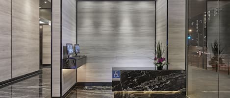 A modern reception area with a marble reception desk, a wheelchair accessibility sign, and a view of the city through a glass wall.