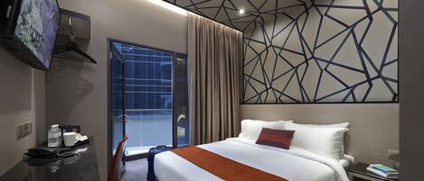 Une chambre d’hôtel comprenant un lit, un bureau avec un téléphone, une chaise, un téléviseur fixé au mur et une fenêtre avec des rideaux.