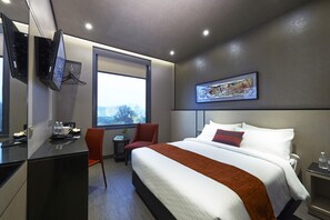 A modern hotel room with a large bed, a desk, a chair, a television, and a window with a city view. - Hotel Boss (Singapore)