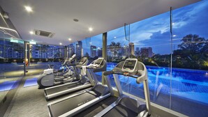 A gym with treadmills, exercise mats, and a view of a cityscape and pool. - Hotel Boss (Singapore)