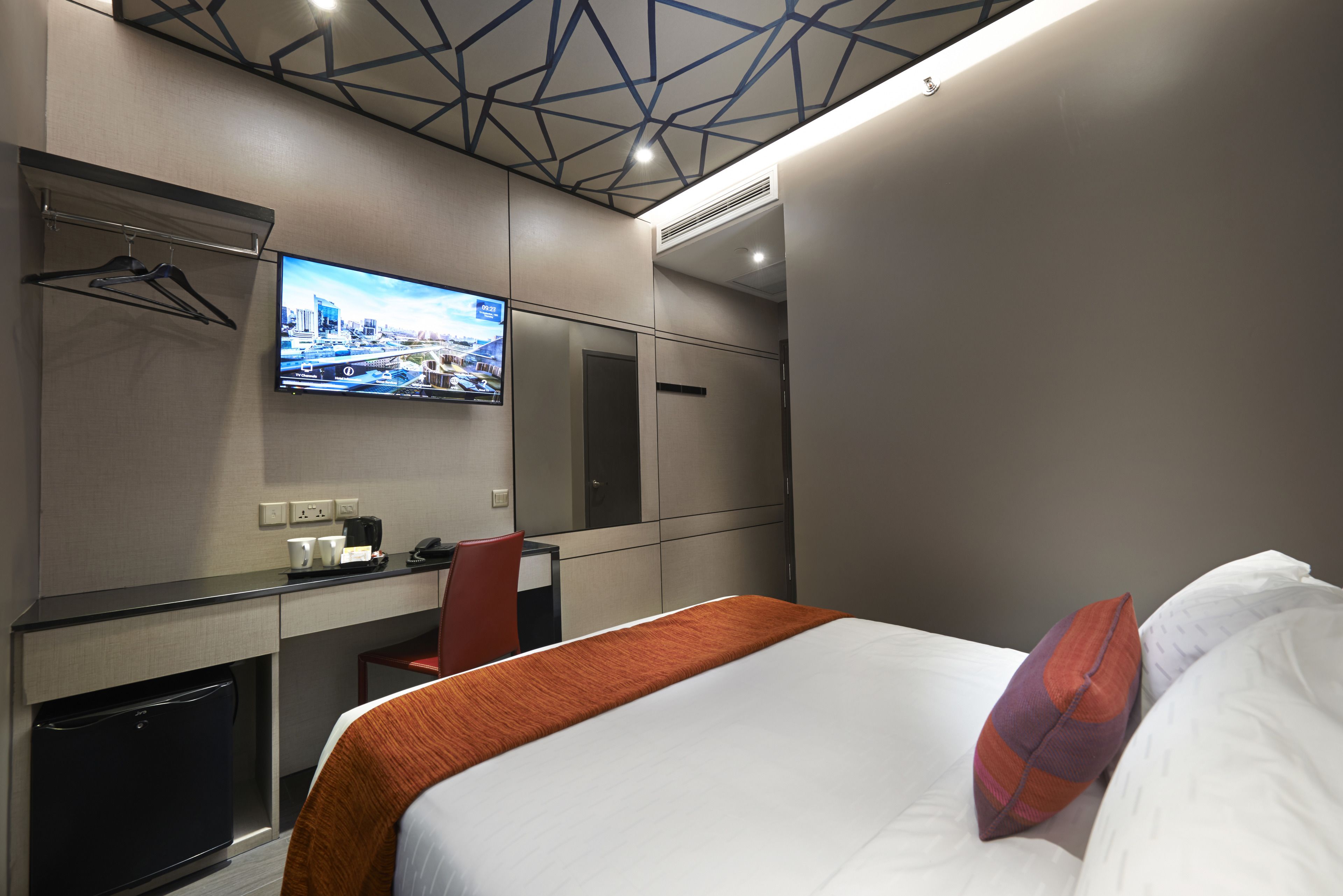 A hotel room with a bed, a desk, a chair, a TV, and a wardrobe.