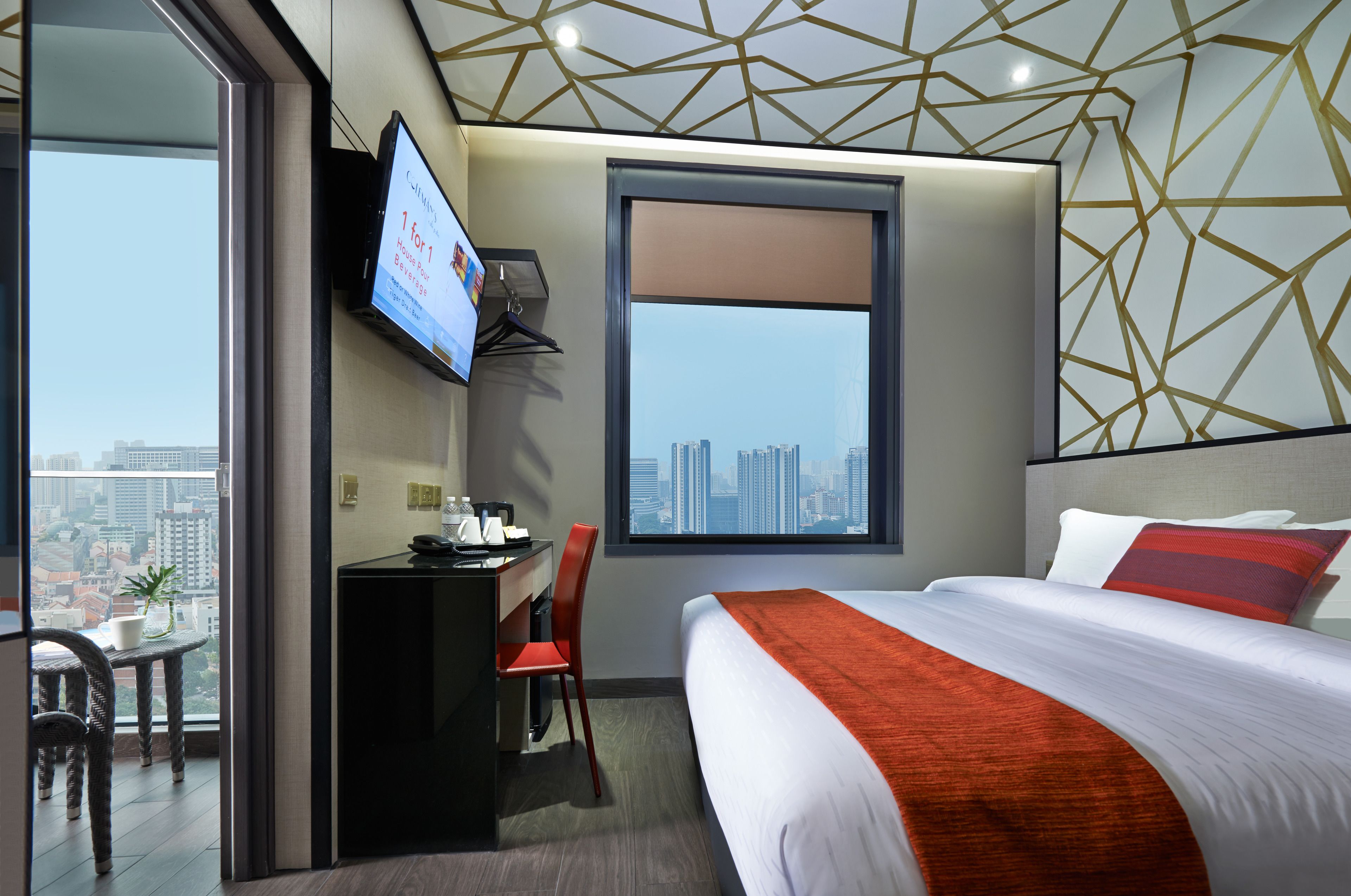 A hotel room with a bed, desk, chair, TV, and a large window with a city view.