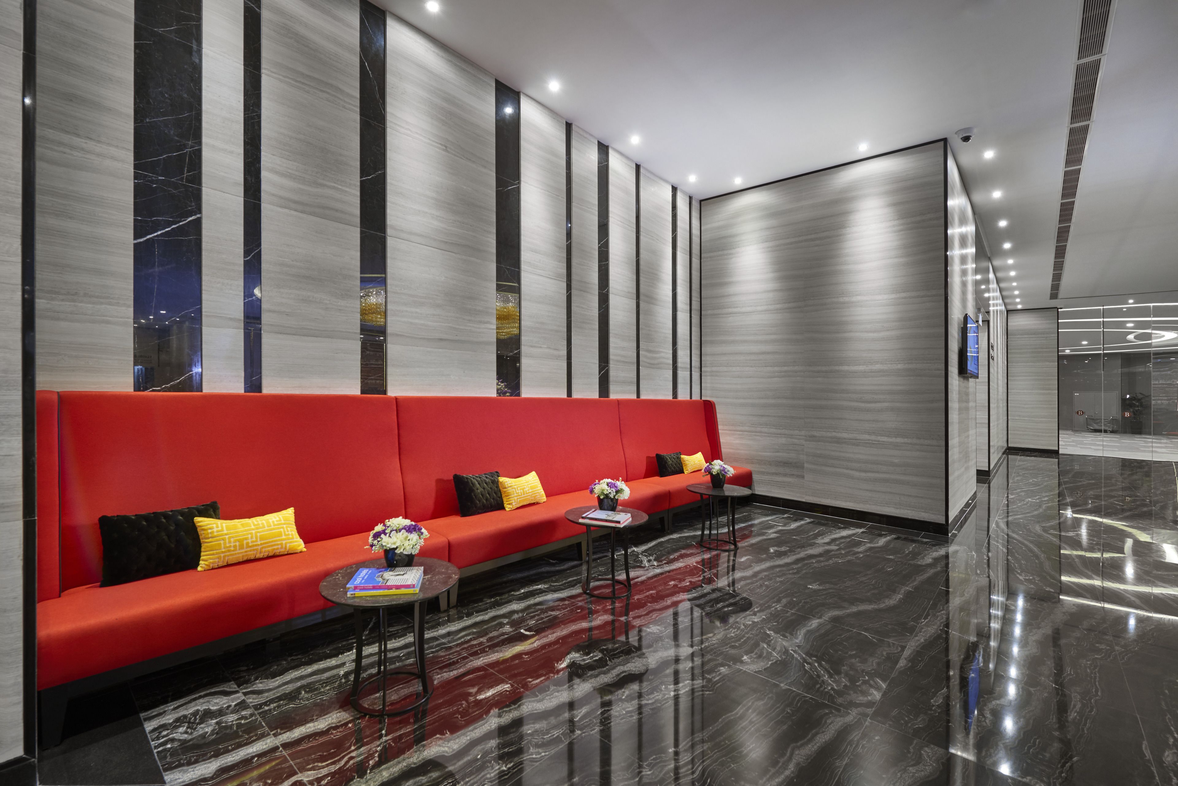 A modern lobby with a red sofa, two small tables, and a marble floor.