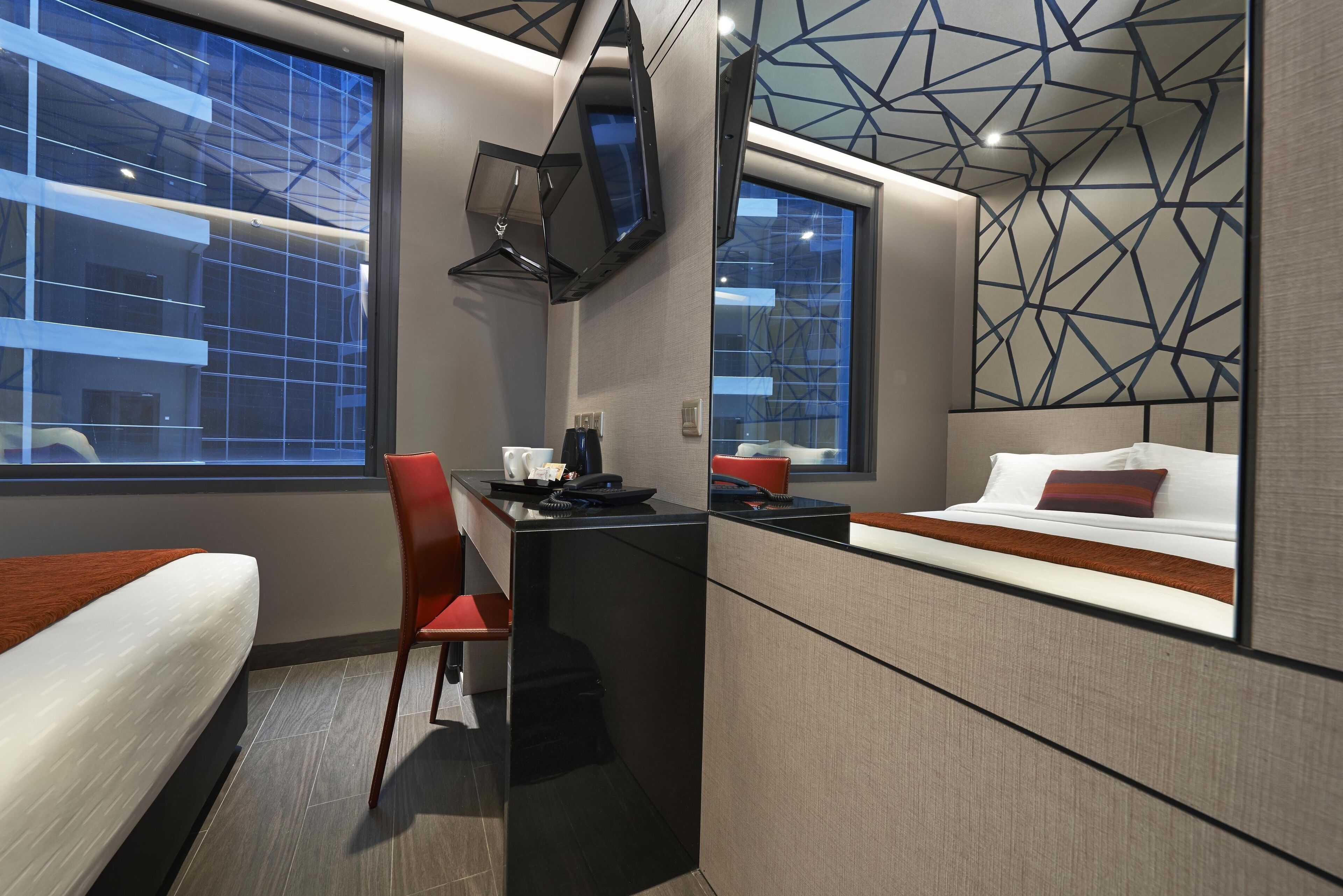 A modern hotel room with a bed, desk, chair, and a large mirror.
